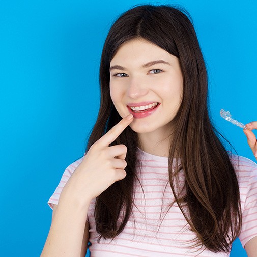 Teenage girl smiling while holding an Invisalign aligner in Columbus