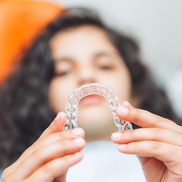 Female patient holding Invisalign aligner in orthodontist chair