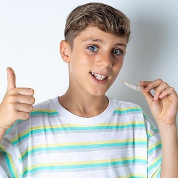 Teen boy holding an Invisalign aligner and giving a thumbs up