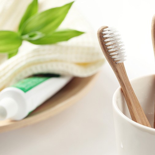 Two toothbrushes in a cup near plate with towel and toothpaste